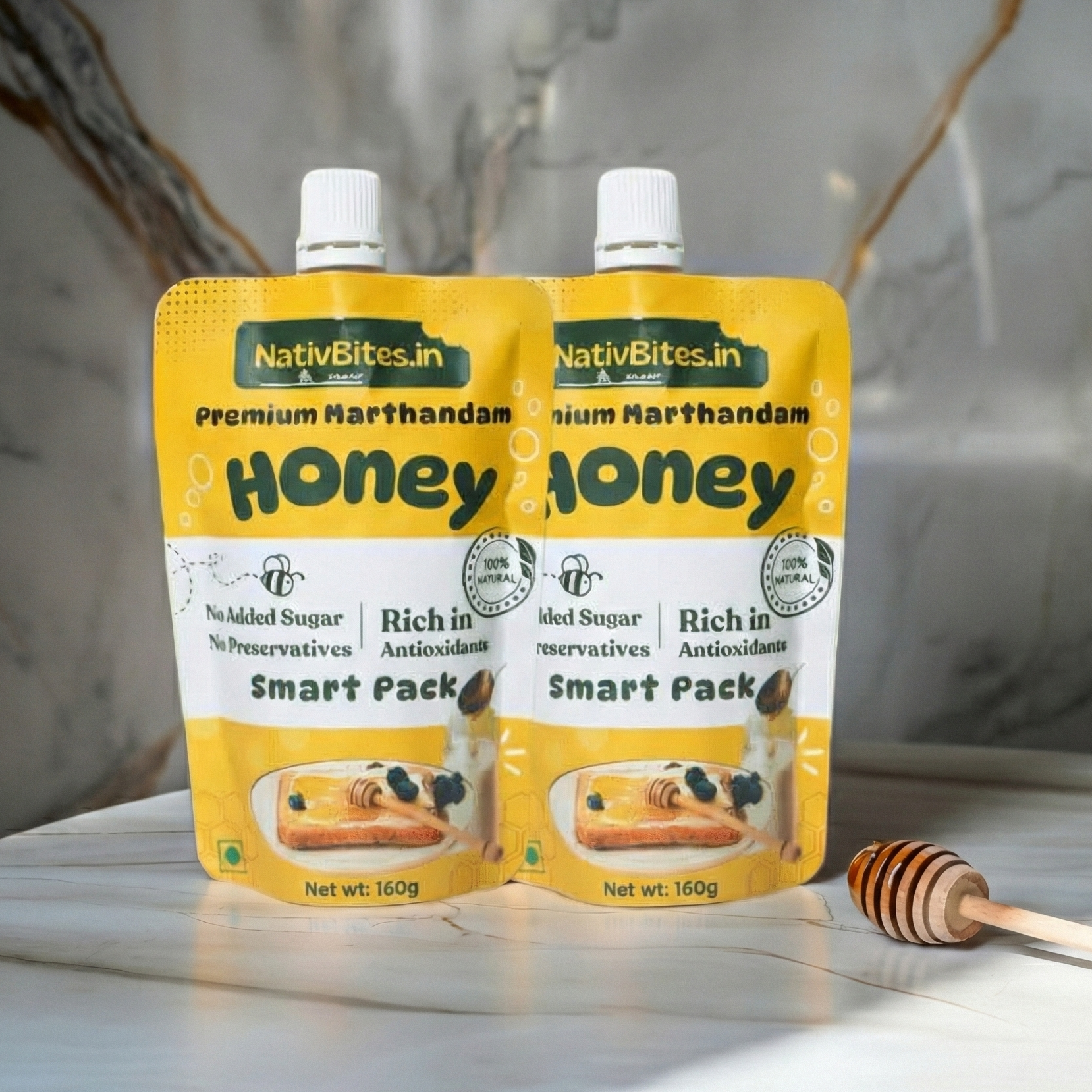 Two packets of NativBites.in honey on a marble surface with a honey dipper.